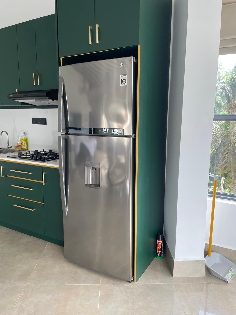Fitted green kitchen with brass handles and a full-size LG stainless-steel fridge freezer