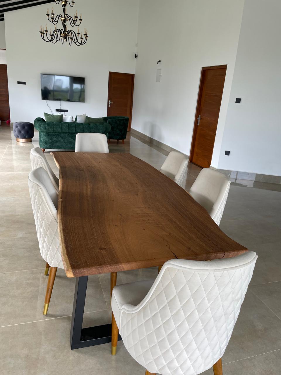Live-edge hardwood dining table with cream quilted chairs beneath a chandelier